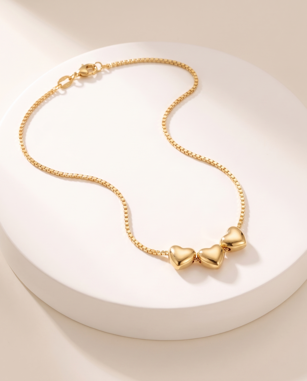 Aria Heart Necklace in gold, delicate box-link chain with a cluster of three small hearts, 18K gold-plated stainless steel with PVD finish, on a white pedestal