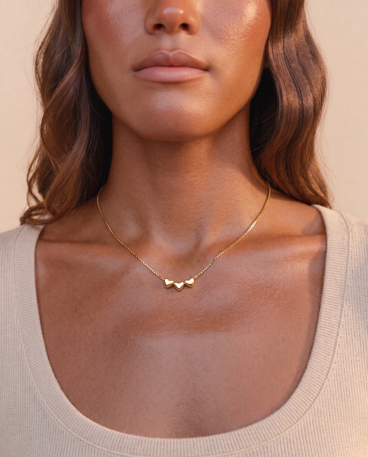 Model wearing the Aria Heart Necklace in gold, three small hearts on a delicate 18K gold-plated stainless steel chain with PVD finish and skin-friendly design