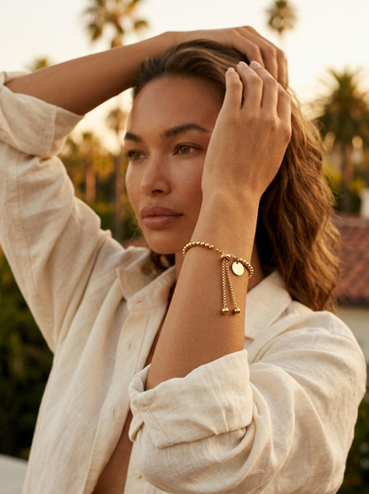 Woman in a cream linen shirt wearing Perla Beaded Bracelet at golden hour with palm trees