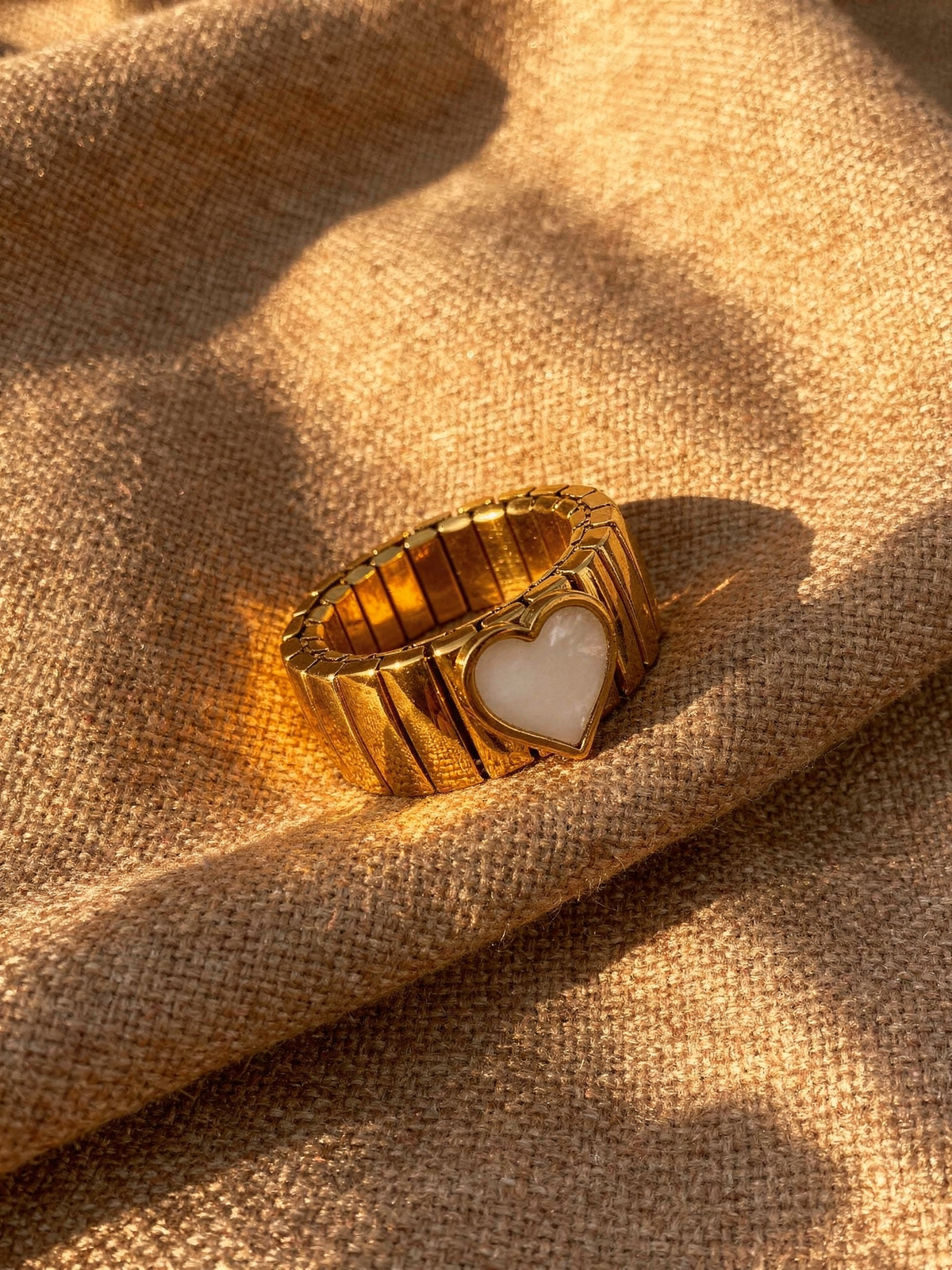 Noa Heart Band Ring in 18k gold-plated stainless steel resting on warm taupe linen at golden hour